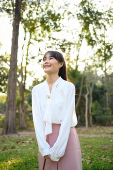 Positive young businesswoman walking in the park in warm sunny summer day.