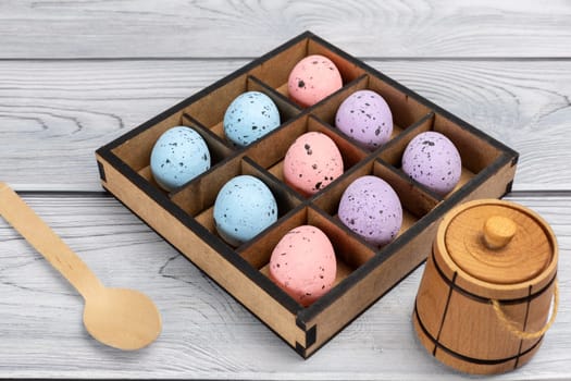 Colorful Easter eggs in a wooden box, a small wooden barrel and a wooden spoon on boards. Top view.