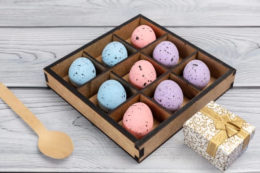 Colorful Easter eggs in a wooden box, a gift box and a wooden spoon on boards. Top view.