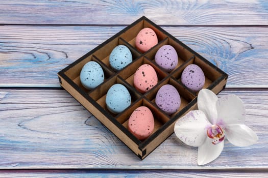 Colorful Easter eggs in a wooden box and an orchid flower on boards. Top view.