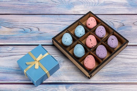 Colorful Easter eggs in a wooden box and a gift box on boards. Top view.