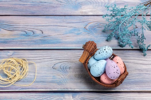 Colorful Easter eggs in a wicker basket, a rope and decoration plants on boards. Top view.