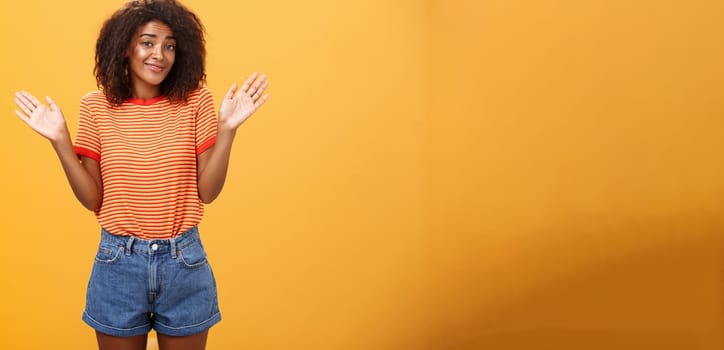 No idea do not care. Careless and indifferent calm happy african american woman with curly hair in summer clothes raising palms and shrugging in uninvolved pose smiling carefree being unaware. Body language concept