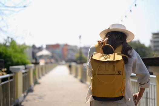 Young female tourist with yellow backpack walking along bridge in Chiang Mai, Thailand.