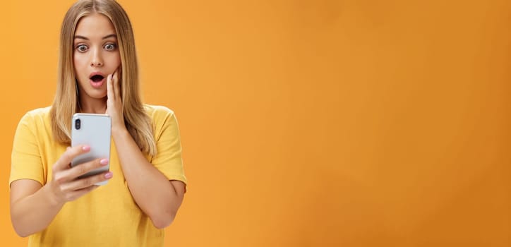 Waist-up shot of shocked and stunned emotive young woman reacting to shocking terrible news reading online from internet gasping opening mouth nervously touchin cheek staring at smartphone screen. Technology concept