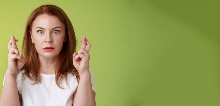 Stunned intense worried middle-aged redhead woman. stare nervously awaiting important result implore dream come true receive positive reply standing stupor green background make wish good luck.