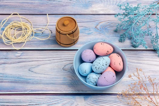 Bowl with colored Easter eggs, a small wooden barrel and a rope on the boards. Top view.