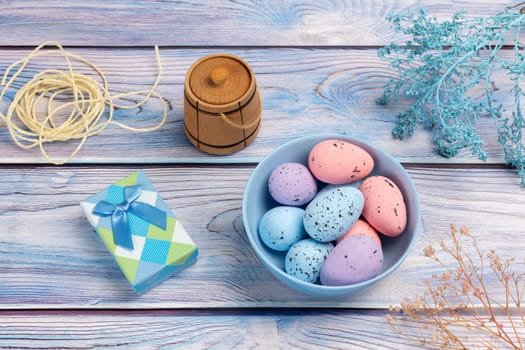 Bowl with colored Easter eggs, a gift box, a small wooden barrel and a rope on the boards. Top view.
