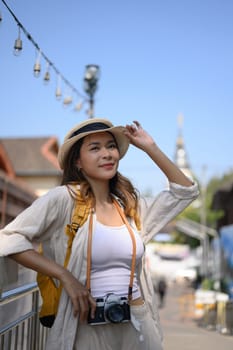 Happy young adult female tourist with backpack standing on bridge in a local city.