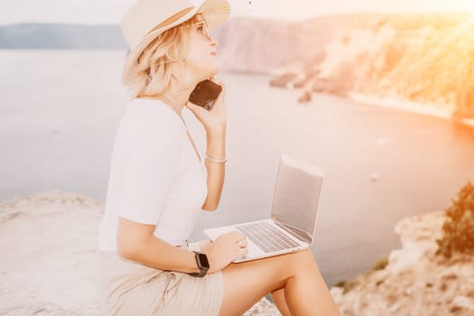 Digital nomad, Business woman working on laptop by the sea. Pretty lady typing on computer by the sea at sunset, makes a business transaction online from a distance. Freelance remote work on vacation