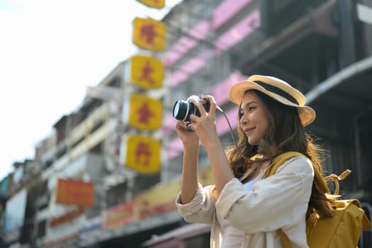 Young female traveller photographing local city street scene with camera.