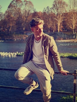 A man is leaning casually on a rail near a body of water, with a relaxed posture. The scene captures a moment of contemplation by the waters edge.