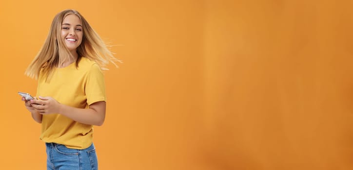 Girl feeling happy receiving message from him. Portrait of carefree charming woman with new haircut waving head standing half-turned, turning to camera with pleased cute smile holding smartphone. Emotions and technology concept