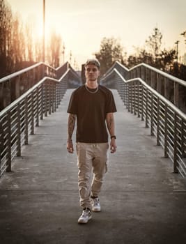 A man wearing a black shirt is walking across a bridge in an urban setting. The mans focused stride is captured as he crosses over the structure.