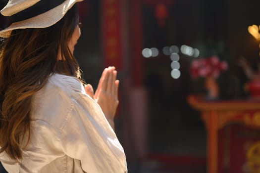 Side view of female tourist praying at a shrine at Chinese temple for blessing, grace and gratitude.