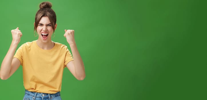 Furious and powerful good-looking emotive woman in yellow t-shirt with gapped teeth yelling in cheer being dedicated fan, supporting favorite team wanting it win raising clenched fists in victory. Copy space