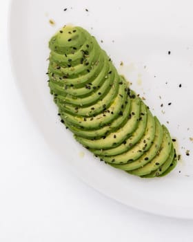 Sliced avocado arranged in a fan shape, sprinkled with black sesame seeds on a ceramic plate