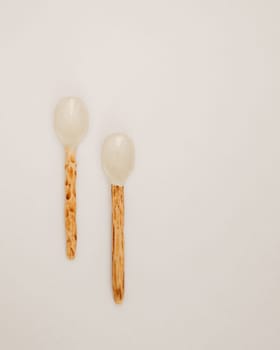 This image features two handcrafted ceramic spoons with rustic wooden handles, laid out on a clean white background