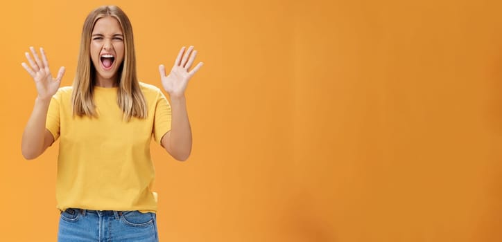 Woman releasing stress yelling with joy and pleasure gesturing with raised arms being daring and rebellious not afraid to show emotions standing passionate and expressive against orange background. Body language concept