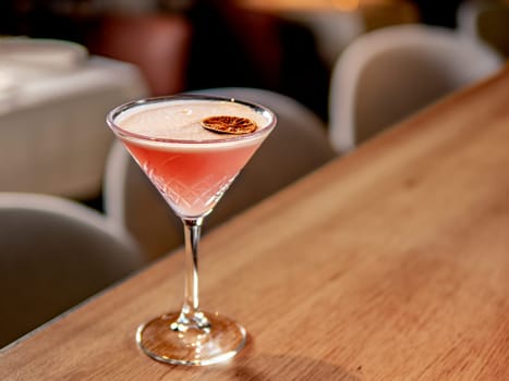Red cocktail in martini glass on bar counter in restaurant interior. Gin alcohol cocktail decorated egg white and dry lichee fruit slice. Pink cold alcoholic cocktail in bar or nightclub background