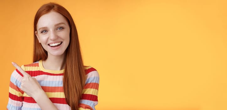 Friendly outgoing good-looking ginger girl university student discussing lecture classmate smiling laughing pointing upper left corner questioned curious know details standing orange background.