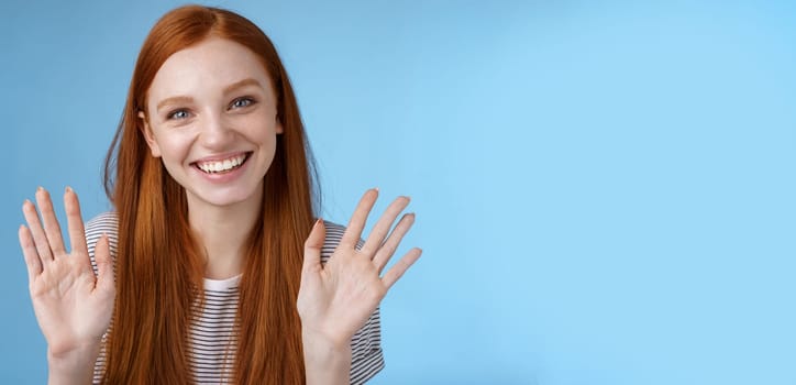 Charming redhead elder sister say goodbye sibling friends smiling cheerful waving raised palms show ten fingers grinning joyfully look carefree relaxed, talking casually blue background.