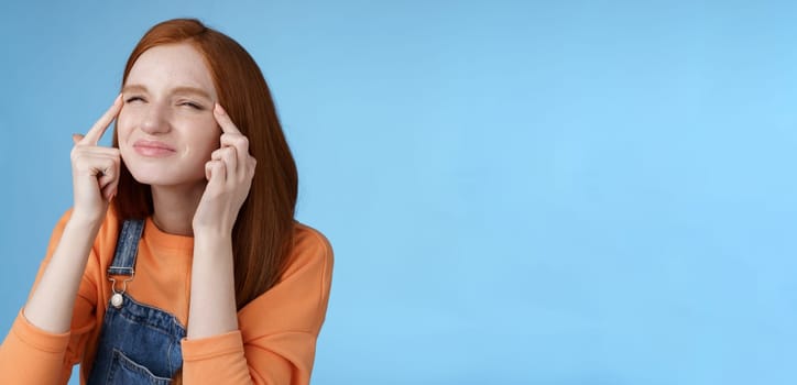 Cute funny european redhead girl forgot glasses trying read sigh stretch eyelids squinting frowning focused look upper left corner perplexed see what happening, standing blue background.