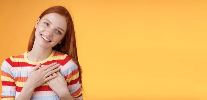 Happy grateful passionate stylish redhead european girl thanking dearest friend lovely sweet gift press palms heart smiling broadly tilting head amused gratefully appreciate, orange background.