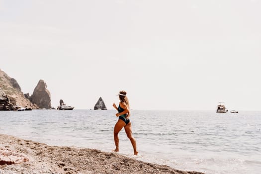 Woman beach vacation photo. A happy tourist in a blue bikini enjoying the scenic view of the sea and volcanic mountains while taking pictures to capture the memories of her travel adventure