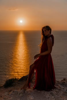 Woman sunset sea red dress, back view a happy beautiful sensual woman in a red long dress posing on a rock high above the sea on sunset