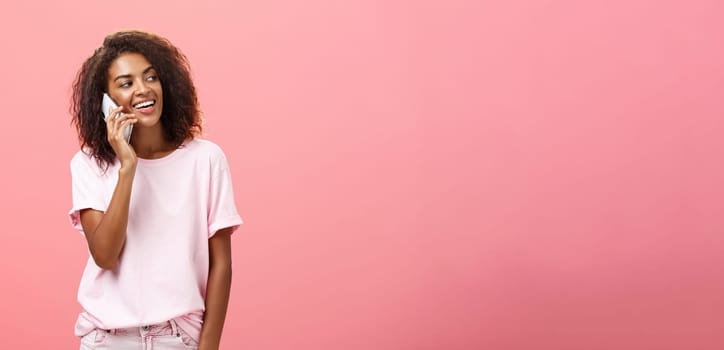 Woman calling boyfriend come pick her up after practice standing on street carefree and chill gazing right with broad satisfied smile holding smartphone near ear posing over pink background. Technology and emotions concept