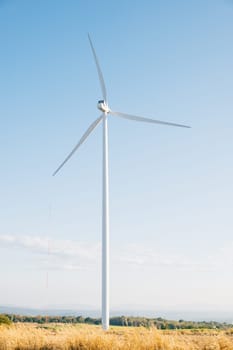 Atop a mountain windmill farm turbines turn in sync with nature generating clean energy. Modern wind technology supporting sustainable development under a serene blue sky.