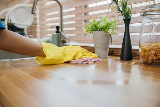Housewife or maid in modern kitchen wipes dining table surface. Using professional cleaning products for home perfect tidiness. Cleaner at work safety glove hygiene routine. Maid housekeeping concept.