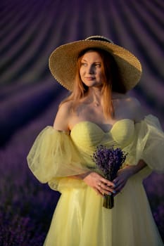 Lavender sunset girl. A laughing girl in a blue dress with flowing hair in a hat walks through a lilac field, holds a bouquet of lavender in her hands