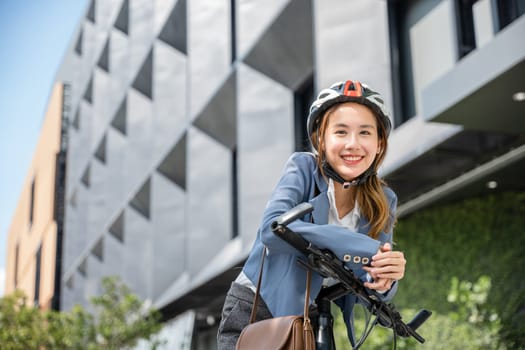 An Asian businesswoman morning commute is a portrait of cheerfulness. She stands with her bicycle helmeted and suited up embodying the modern concept of a joyful business commuter.
