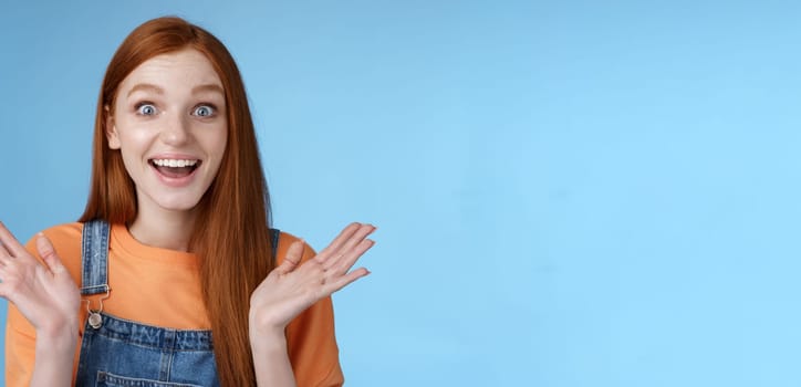 Surprised delighted happy friendly-looking amused redhead female friend learn incredible good news congratulating girlfriend fascinated wide eyes camera joyfully clap hands amazed, blue background.