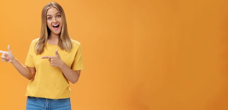 Check out copy sapce of dream. Upbeat good-looking pleasant female shop assistant in t-shirt pointing left with finger guns and smiling amused at camera recommending to watch that direction. Advertisement concept