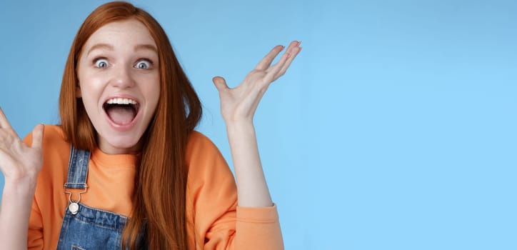 Surprised astonished sensitive overwhelmed young happy redhead girl receive incredible fantastic prize wide eyes astonished raising hands triumphing win lottery celebrating joyfully.