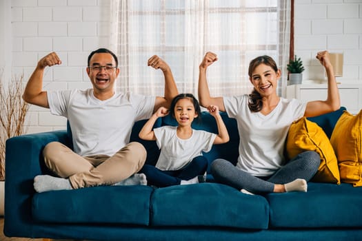 In their cozy living room at home young parents mom and dad join their child and daughter in showcasing biceps muscles symbolizing family strength and togetherness on this special Family Day.