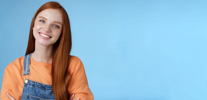 Charismatic kind pleasant redhead girl blue eyes smiling friendly listen politely customer standing blue background tilting head amused grinning cross hands chest professional confidence pose.