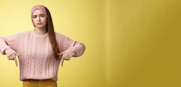 Why me, gosh. Gloomy upset complaining cute glamout young european girl in casual sweater, headband frowning, whining grimacing displeased pointing down, unhappy see lots work over yellow wall.