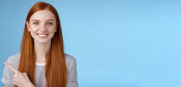 Pleasant charismatic helpful friendly-looking female redhead blue eyes pointing left index finger help make decision pick product store smiling broadly confident gaze camera asking trust her. Lifestyle.