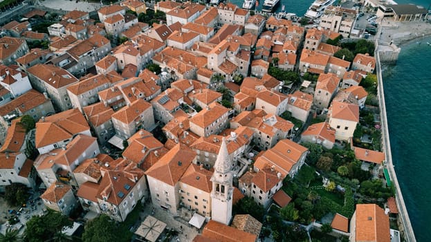 White bell tower of the Church of St. Ivan among the red roofs of the ancient houses of Budva. Montenegro. Drone. High quality photo