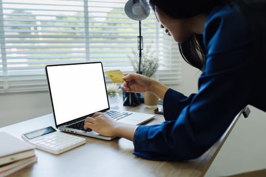 Young woman makes a purchase on the Internet on the laptop with credit card and mockup laptop blank screen.