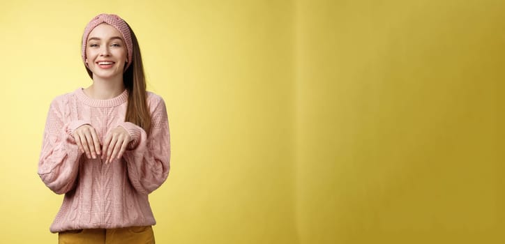 Girl pretends easter bunny. Charming cute female in knitted sweater holding palms like rabbit smiling happily, mimicking pretty animal fooling around from happiness and joy against yellow background.