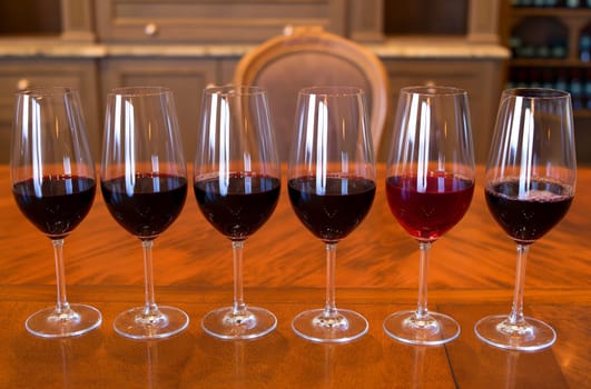 A row of glasses filled with red wine of different shades on a polished wooden table