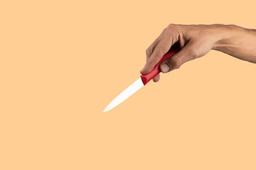 Black male hand holding a red cooking knife isolated on orange peach background. High quality photo