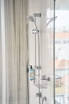 A shower stall with a glass shower door, metal handle, and composite material shower bar featuring a shower head and soap dispenser