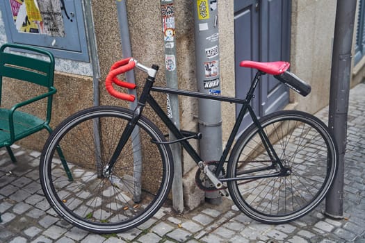 A black bicycle with vibrant red handlebars is resting on a cobblestone street, showcasing its sleek design and unique color contrast