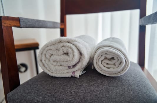 A pair of rolled hardwood towels are placed on a wooden chair, resembling a spiral pattern. The towels sit in a rectangular shape on the chair in a room with wooden flooring
